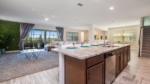 A modern kitchen with a central island, a dining area with a table and chairs, and a living room with a sofa and a large window. - Solara Resort 9 Bedroom 6 Bathroom Resort Villa (Kissimmee)