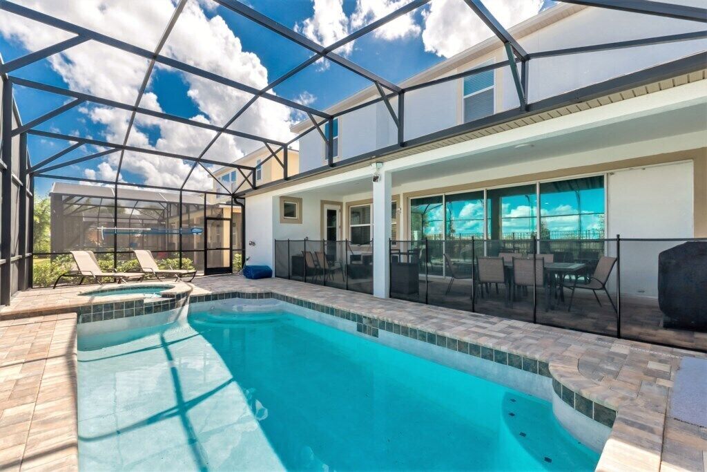 Une piscine dotée d’une structure en verre, de chaises longues et d’un espace patio aménagé avec du mobilier d’extérieur.