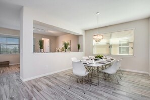 A dining area with a round table, white chairs, and a chandelier. - Solara Resort 9 Bedroom 6 Bathroom Resort Villa (Kissimmee)