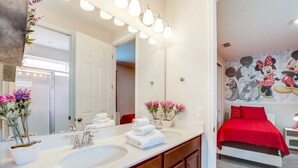A bathroom with a large mirror, two sinks, and a red bed in the adjacent room. - Solara Resort 9 Bedroom 6 Bathroom Resort Villa (Kissimmee)