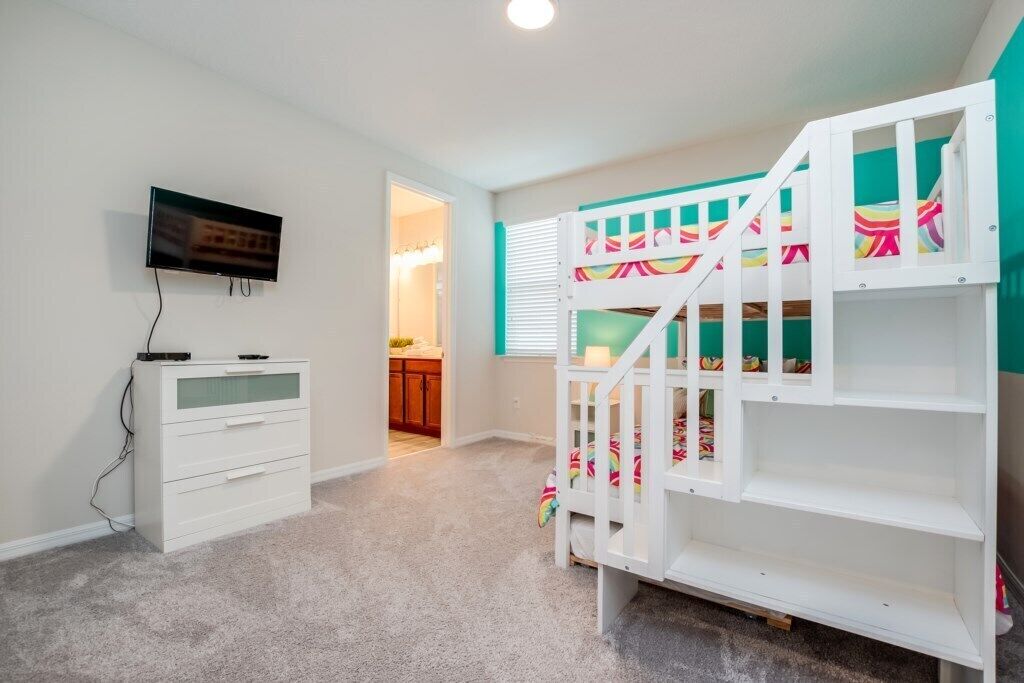 Un dormitorio infantil con literas, televisor y cómoda blanca.