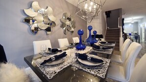Un espace repas agrémenté d’un lustre moderne, d’œuvres d’art murales abstraites et d’une table à manger élégamment dressée, avec des chaises blanches et des vases bleus.