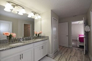 A bathroom with a double sink vanity, a large mirror, and a shower area.
