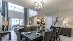A spacious dining area with a high ceiling, modern chandelier, and a view of the adjacent living room. - 5 Bdrm Champions Gate Luxury Villa (Davenport)