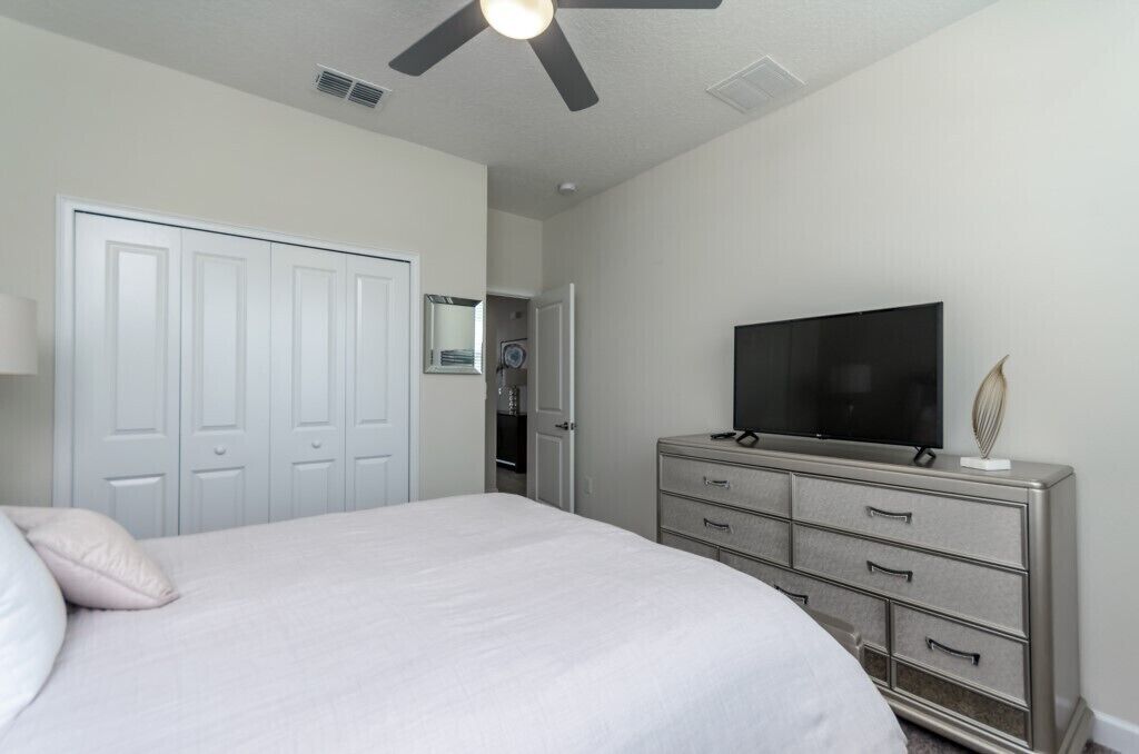 A bedroom with a bed, a dresser, a television, and a ceiling fan.