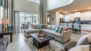 A spacious living room with a large sofa, a coffee table, and a view of the outside. - 5 Bdrm Champions Gate Luxury Villa (Davenport)