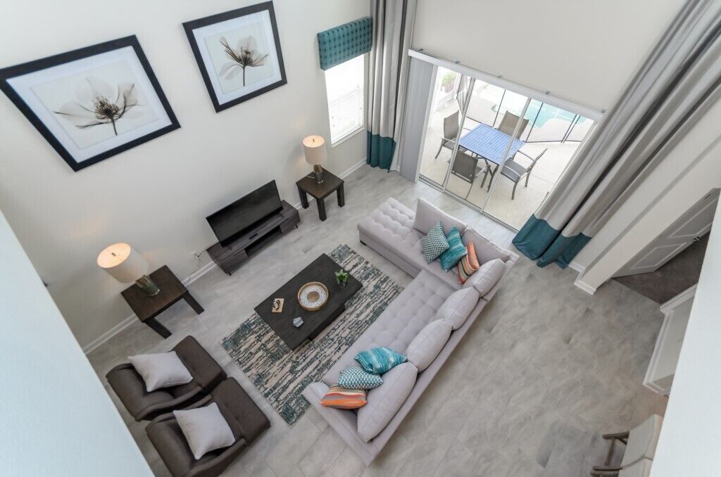 A modern living room with a sofa, coffee table, and side tables. There are framed pictures on the wall, a window with curtains, and a view of the outside patio.