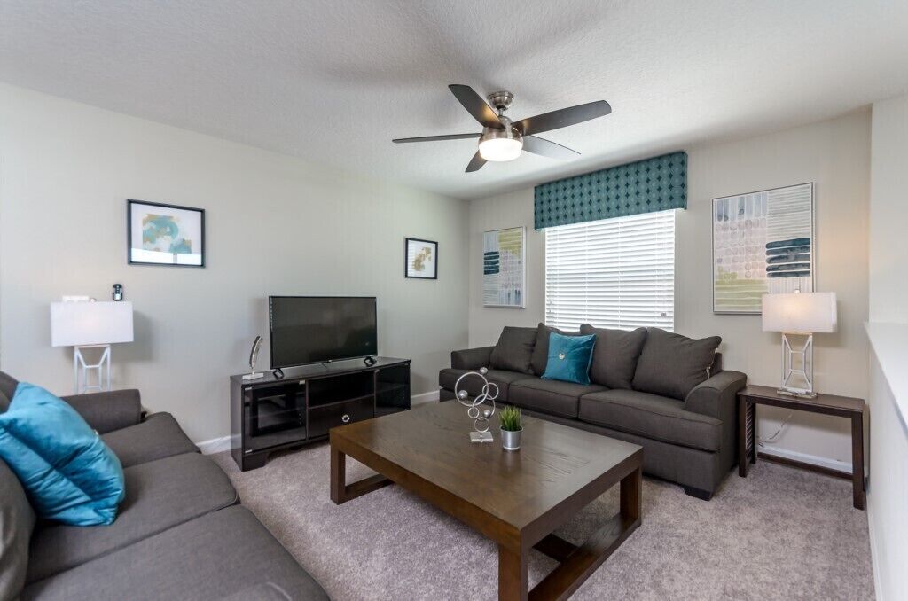 Ein modernes Wohnzimmer mit Fernseher, Deckenventilator, Sofa, Couchtisch und Lampe.