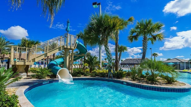 A pool area with a water slide, palm trees, and a clear blue sky. - 5 Bdrm Champions Gate Luxury Villa (Davenport)