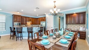 A spacious kitchen with wooden cabinets, a central island, and a dining area set for six with blue tableware. - Ultimate 5 Bed 5 Ba Villa with Game Room, Pool & Spa - Ihr4021 (Kissimmee)
