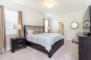 A bedroom with a large bed, a nightstand, a dresser, a mirror, and a television.