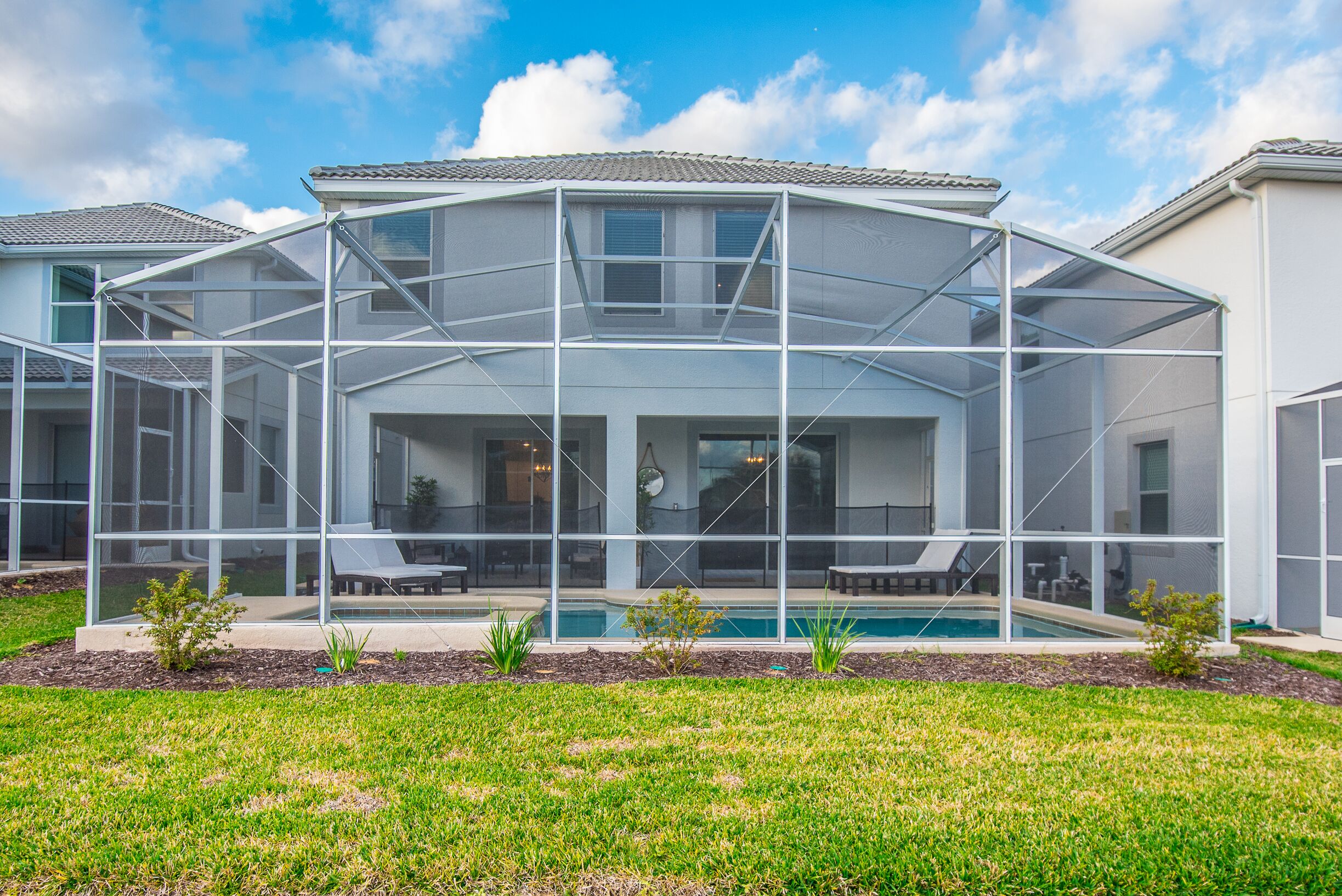 A modern house with a covered patio, a swimming pool, and a well-maintained lawn.