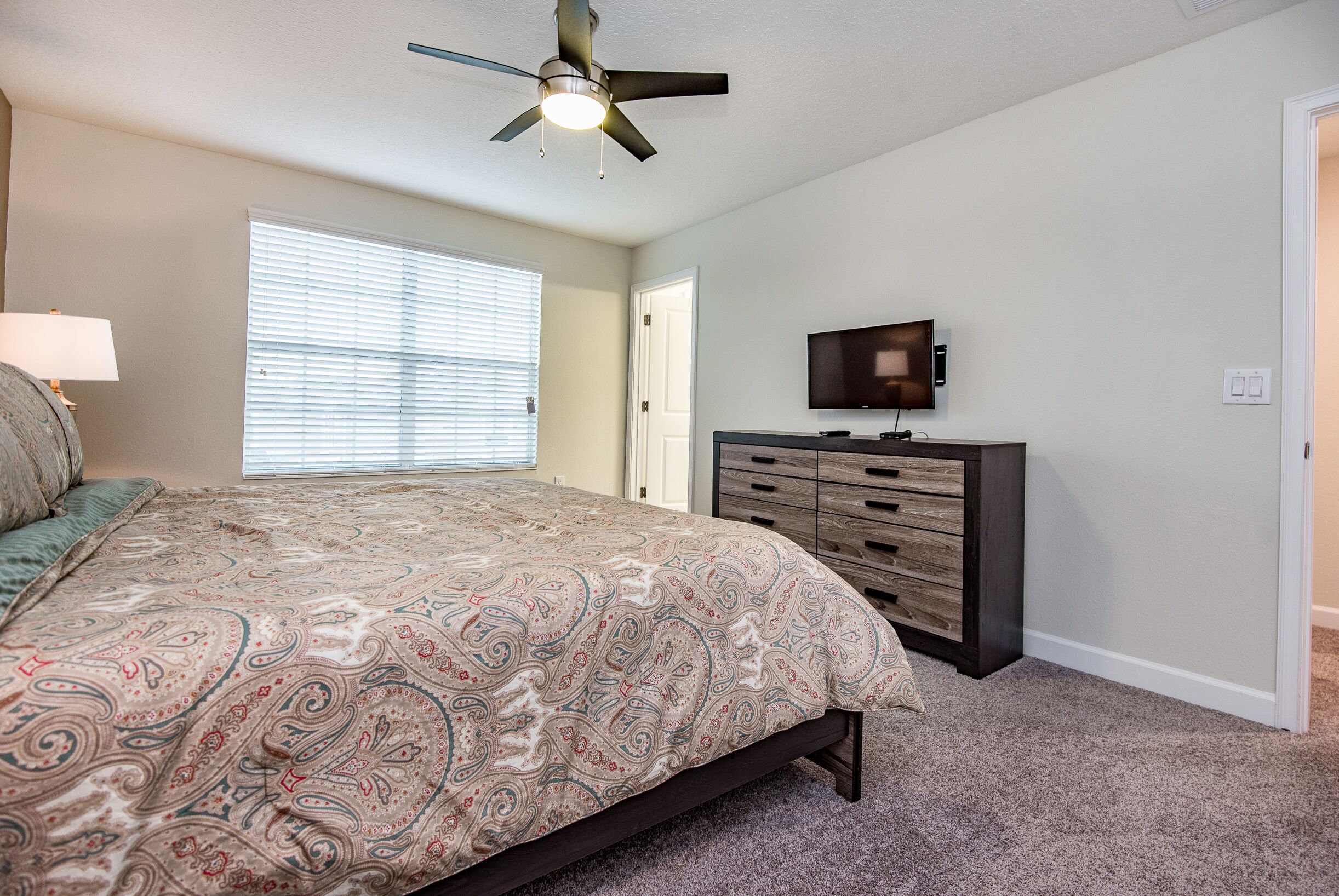 Une chambre à coucher avec un lit, un ventilateur de plafond, une commode et un t éléviseur.