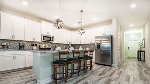 A modern kitchen with white cabinets, a central island with bar stools, stainless steel appliances, and a herringbone-patterned floor. - 6 Bedroom Villa W Private Pool & Game Room (Davenport)