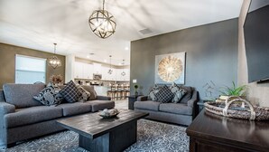 A modern living room with two grey sofas, a wooden coffee table, patterned rug, and a kitchen in the background. - 6 Bedroom Villa W Private Pool & Game Room (Davenport)