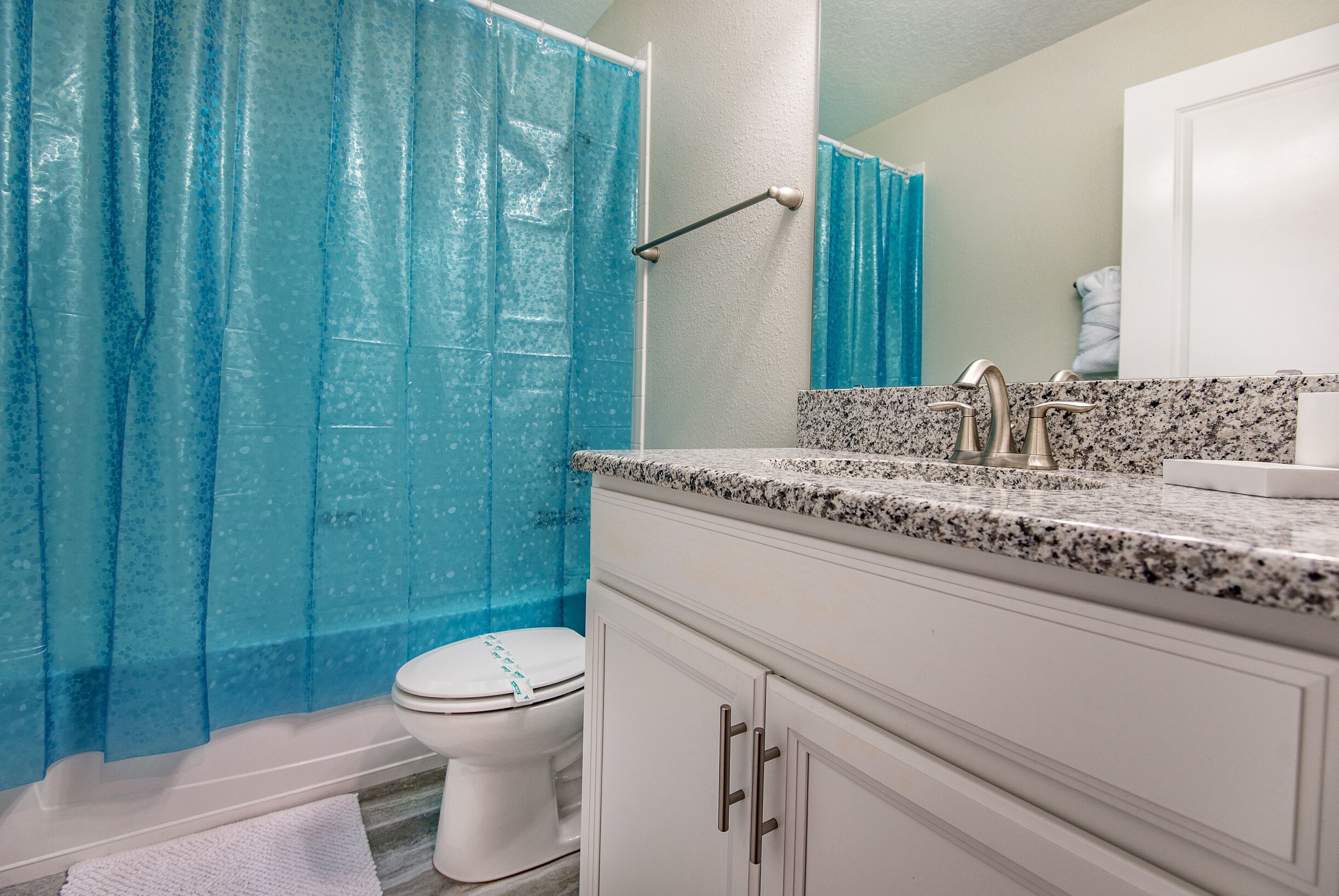 A bathroom with a white toilet, a granite countertop, and a blue shower curtain.