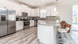 A modern kitchen with white cabinets, stainless steel appliances, a granite countertop, and a bar area with stools. - 6 Bdrm 5 BA Vacation Home (Davenport)