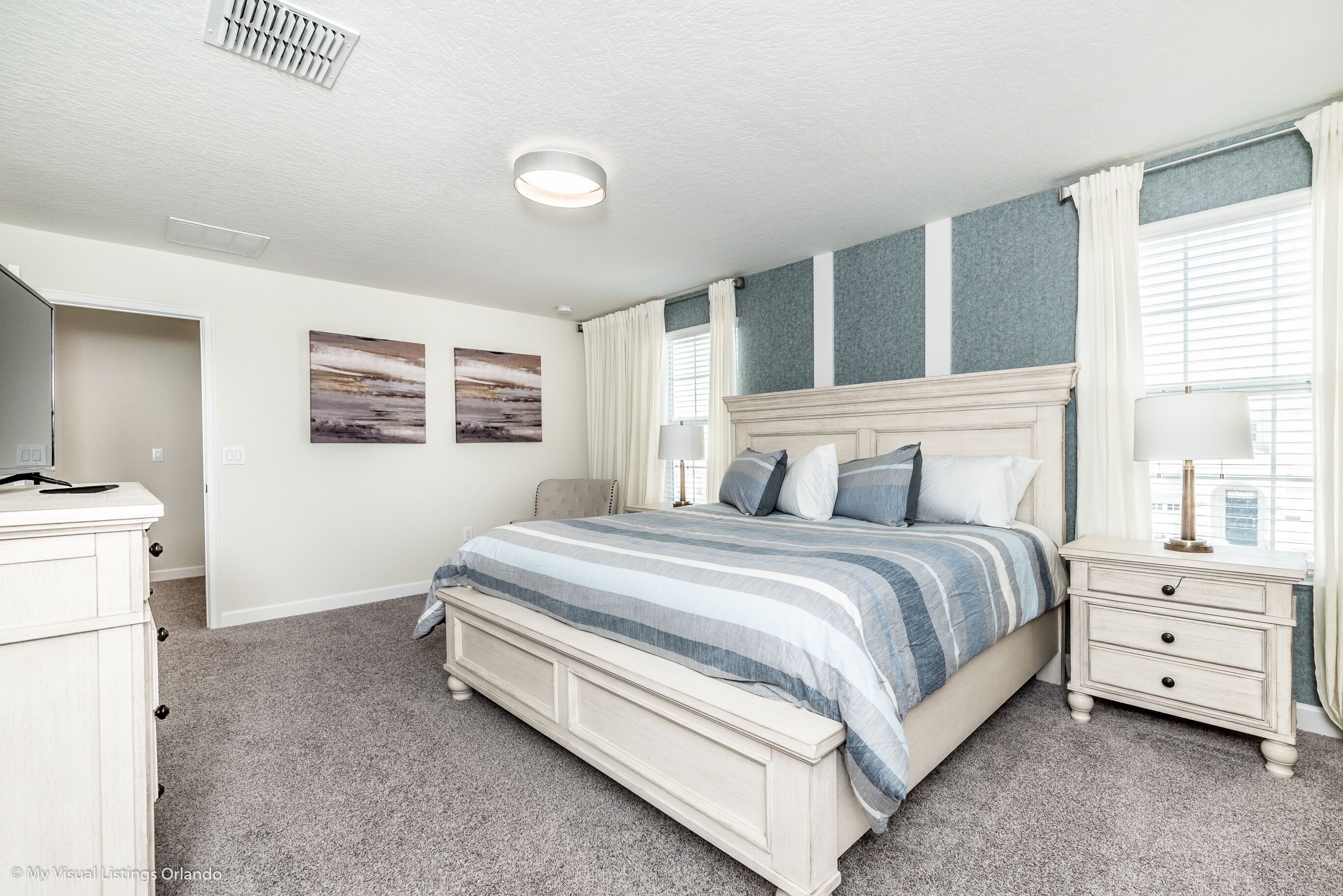 A bedroom with a bed, nightstands, a dresser, and artwork on the walls.