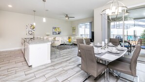 A spacious kitchen with a central island, a dining area with a modern chandelier, and a view of the outdoors through large windows. - 3081juliet (Kissimmee)