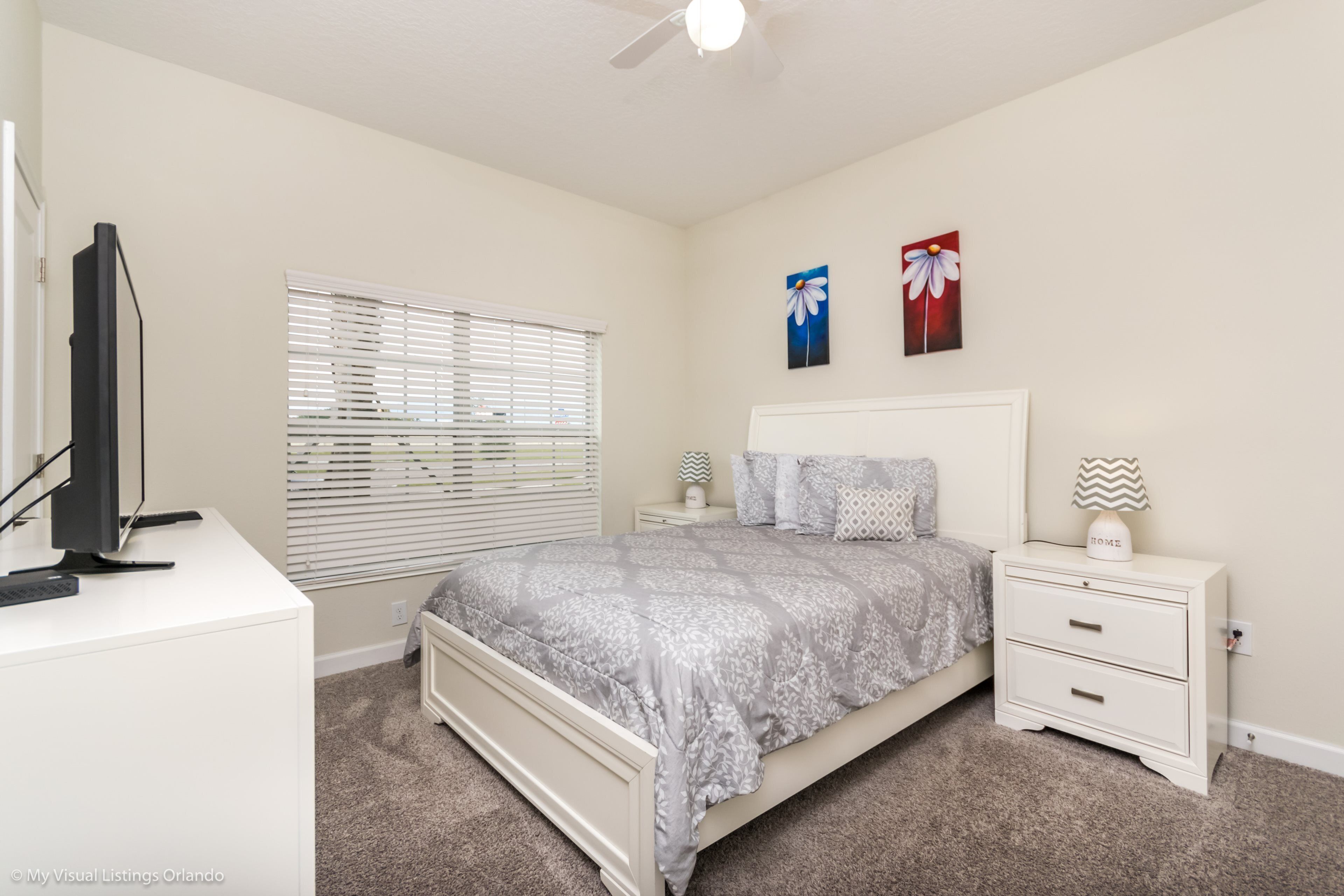 A bedroom with a bed, nightstands, a desk, and a ceiling fan.