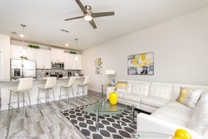Uma sala de estar moderna com uma mesa de centro de vidro, sofá branco e uma área de refeições com banquetas.
