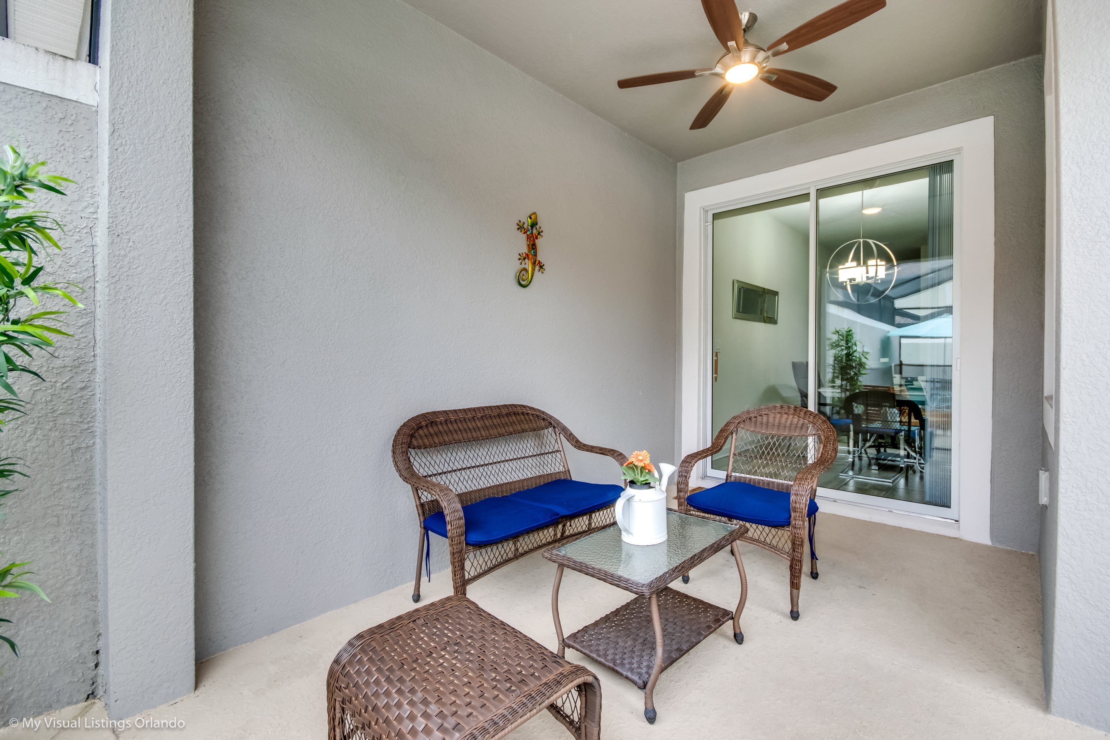 A balcony with wicker furniture, a ceiling fan, and a view of the interior through a glass door.