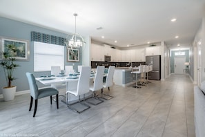 A modern kitchen with white cabinetry, a central island, and a dining area with white chairs and a glass table.
