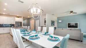 A modern kitchen with white cabinets, a dining area with a white table set for six, teal chairs, and a ceiling fan. - Amazing 6 Bedroom 5 BA Majesty Model (Davenport)