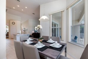 A modern dining area with a rectangular table set for four, surrounded by chairs. A pendant light hangs above the table, and a large window provides natural light.
