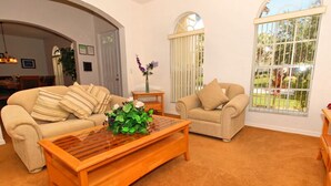 A living room with two beige sofas, a wooden coffee table, and a window with a view of greenery. - Birkdale Pool House (Davenport)