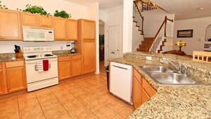 A kitchen with wooden cabinets, a white stove, a microwave, granite countertops, and a stainless steel sink. - Birkdale Pool House (Davenport)