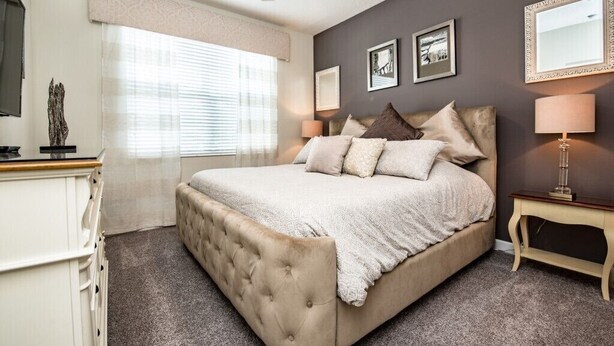 A bedroom with a large bed, a ceiling fan, a window with blinds, and a bedside table with a lamp. - 5 Bed Storey Lake Villa with Games & Pool (Kissimmee)