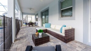 A covered patio area with a wicker sofa, a coffee table, and a dining table. - Ultimate 8 Bedroom Champions Gate (Davenport)