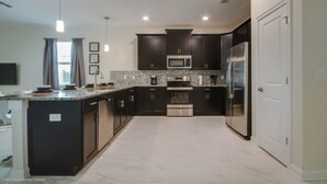 A modern kitchen with dark cabinetry, stainless steel appliances, and a granite countertop. - Ultimate 8 Bedroom Champions Gate (Davenport)