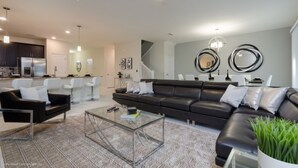 A modern living room with a black leather sofa, a glass coffee table, and a staircase leading to a kitchen area. - Ultimate 8 Bedroom Champions Gate (Davenport)