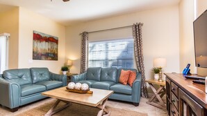 A living room with two blue leather sofas, a wooden coffee table, and a TV on a wooden cabinet.