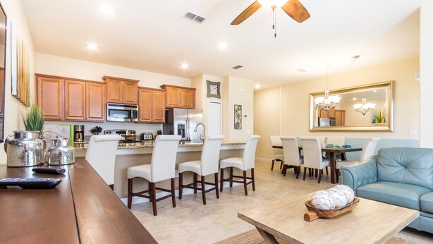 A modern kitchen with wooden cabinets, stainless steel appliances, and a dining area with white chairs and a blue sofa.