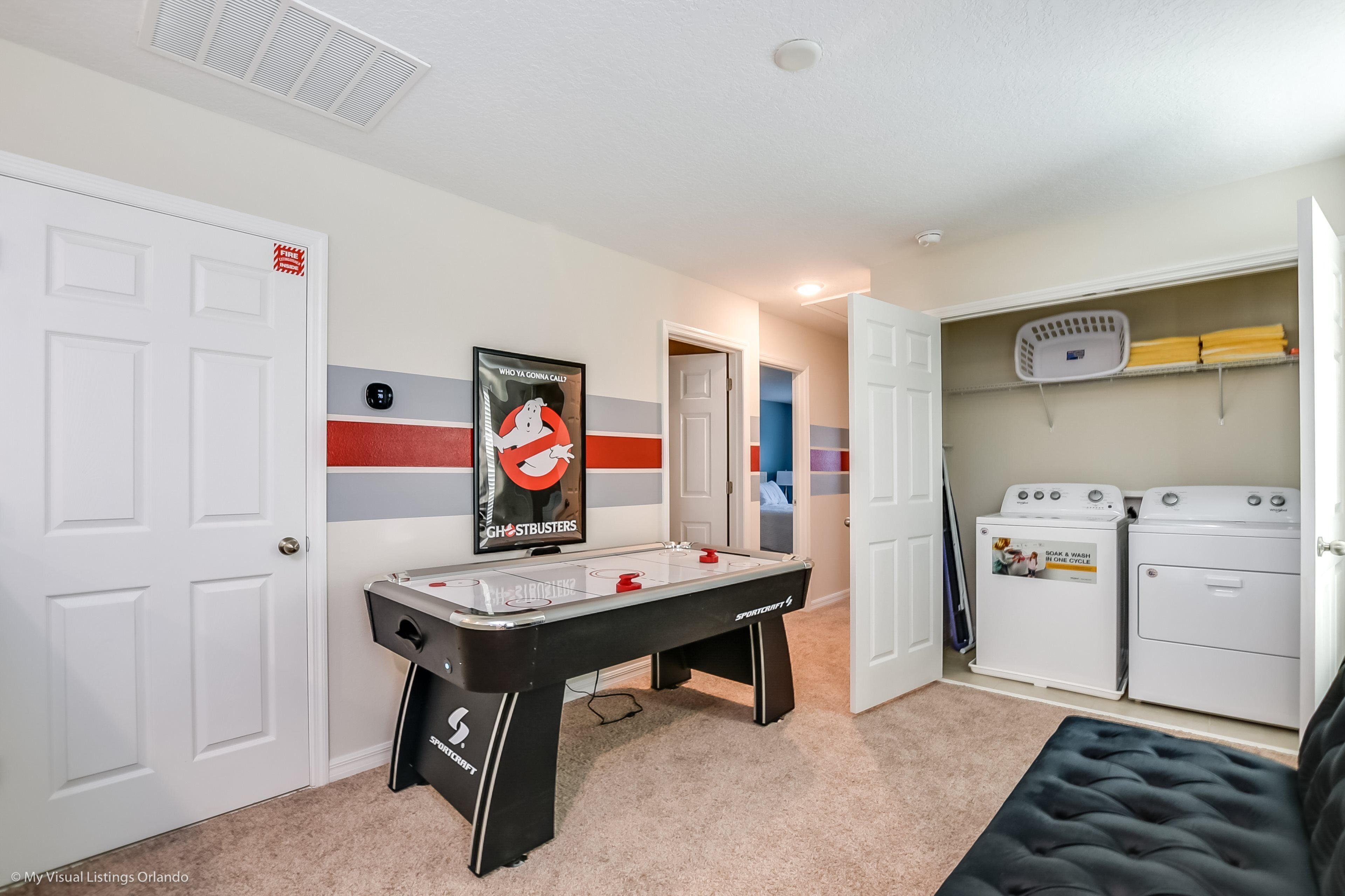 A room with a foosball table, a poster, a laundry area, and a door with a fire exit sign.