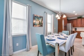 Un comedor con una mesa dispuesta para cuatro personas, sillas azules y una araña.