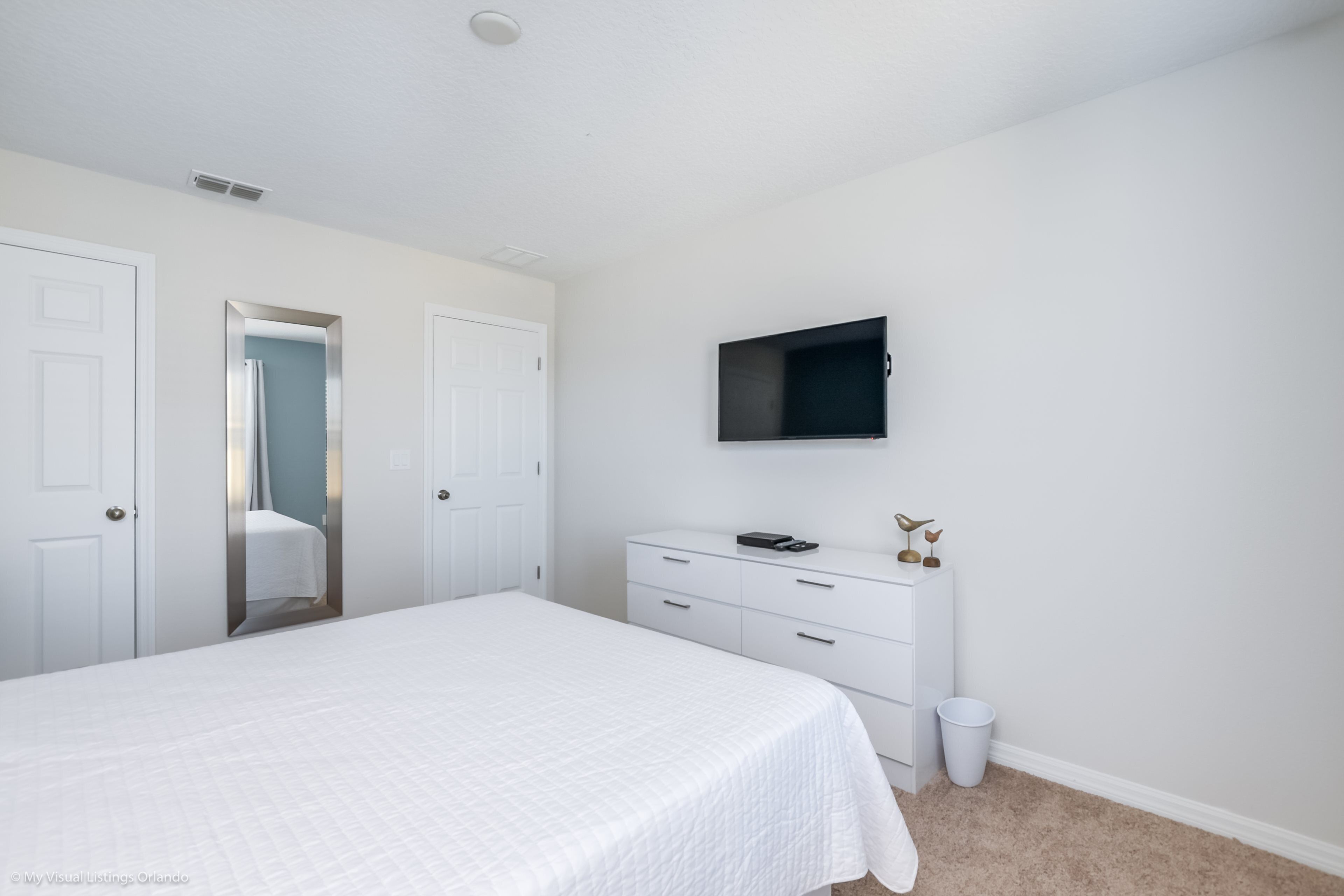 Une chambre à coucher avec un lit, une commode, un téléviseur et une porte.