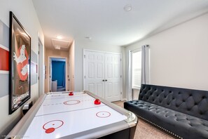 Una habitación con mesa de juego de salón, sofá negro con capitoné y una puerta que da a otra estancia.