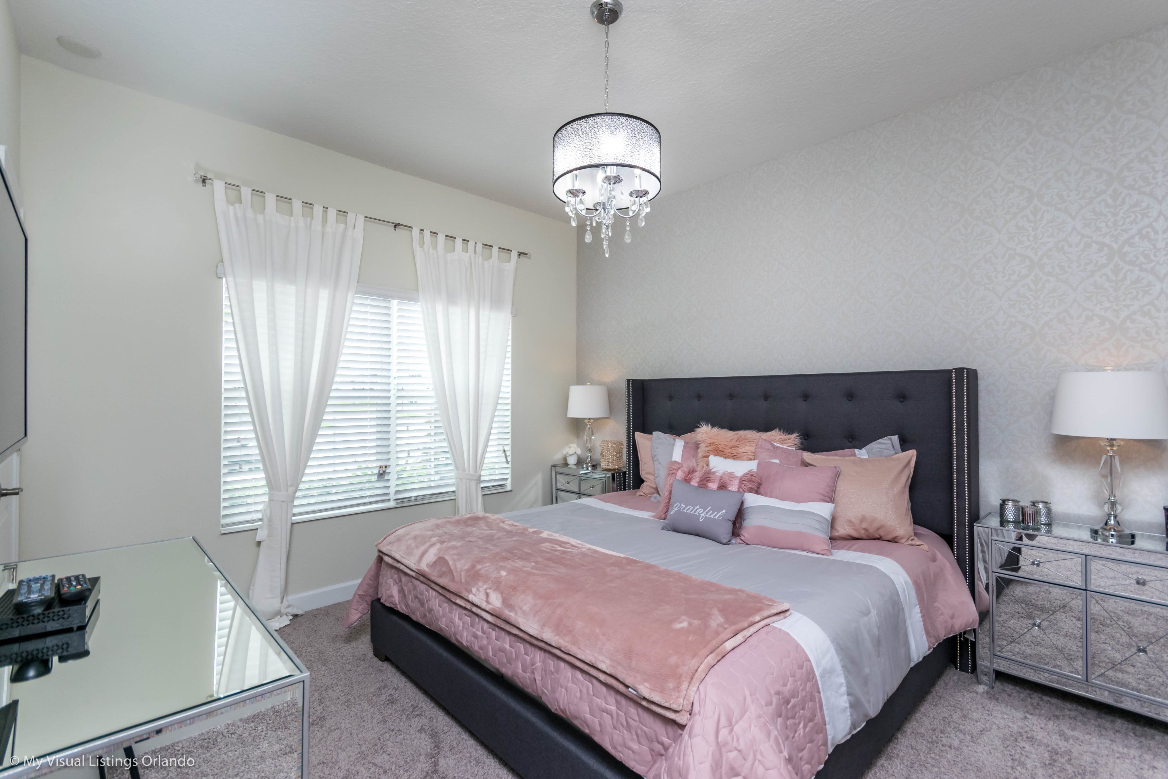 A bedroom with a large bed, bedside tables, a glass desk, and a chandelier.