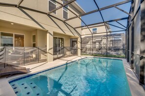 Une piscine intérieure avec des parois en verre transparent, un sol carrelé et un patio ensoleillé agrémenté de mobilier d’extérieur.