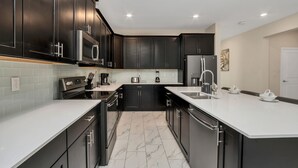 A modern kitchen with dark cabinetry, a large island, and a tiled backsplash.