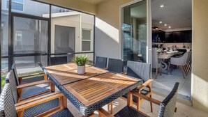 A patio with a wooden table and chairs, a potted plant, and a sliding glass door leading to a kitchen area.