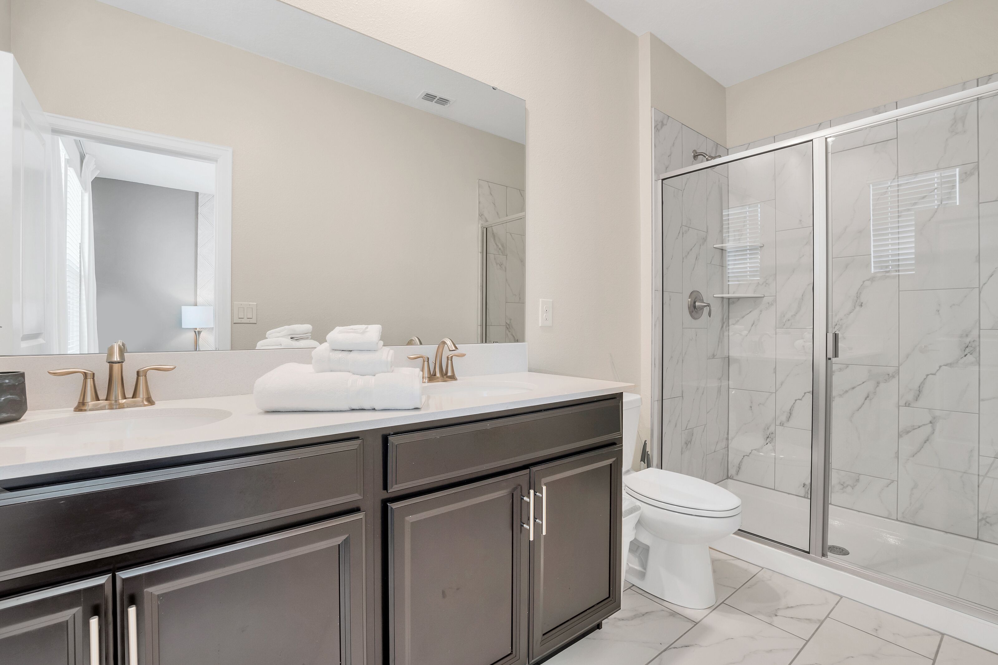 A modern bathroom with a large mirror, a white sink, dark cabinets, and a glass-enclosed shower.