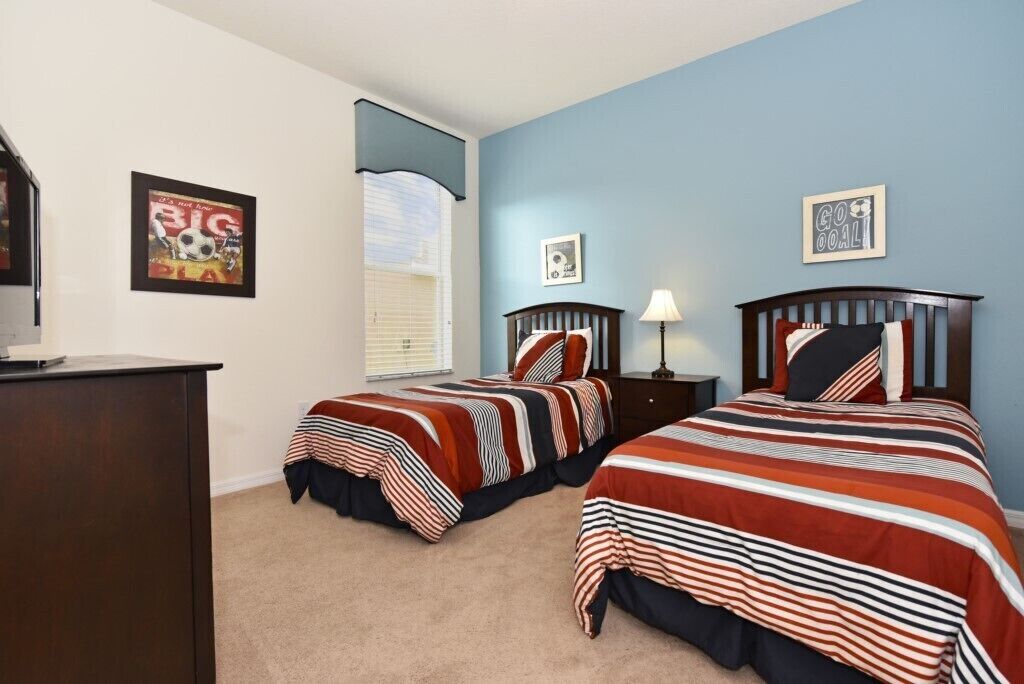 A bedroom with two beds, a desk, and a window with blinds.