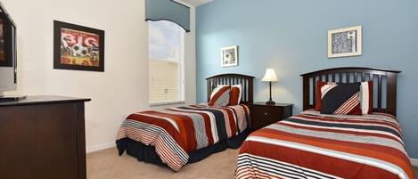 A bedroom with two beds, a desk, and a window with blinds.