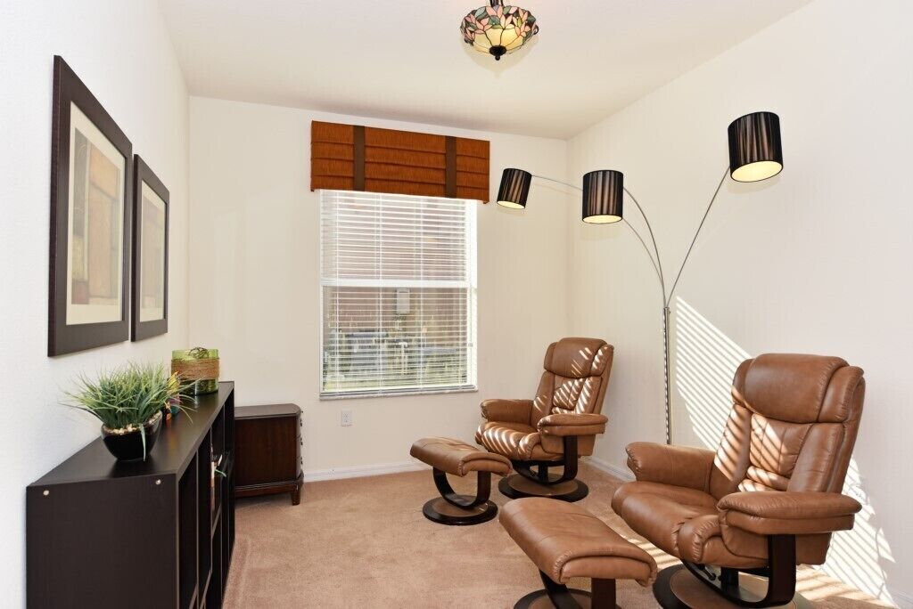 Une pièce comprenant un fauteuil inclinable en cuir marron, un pouf assorti, une console en bois foncé et un lampadaire.