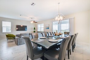 A modern dining area with a glass table, grey chairs, and a chandelier. - 9 Bedroom Champions Gate Resort (Davenport)